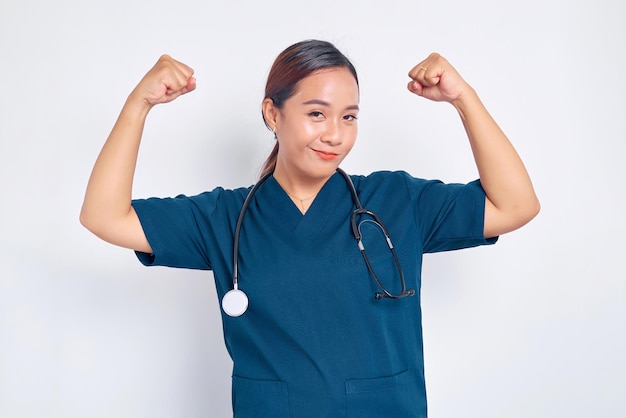 Lächelnde junge asiatische weibliche professionelle Krankenschwester, die in blauer Uniform arbeitet und Muskel und Bizeps zeigt, die stark isoliert auf weißem Hintergrund sind. Healthcare-Medizin-Konzept