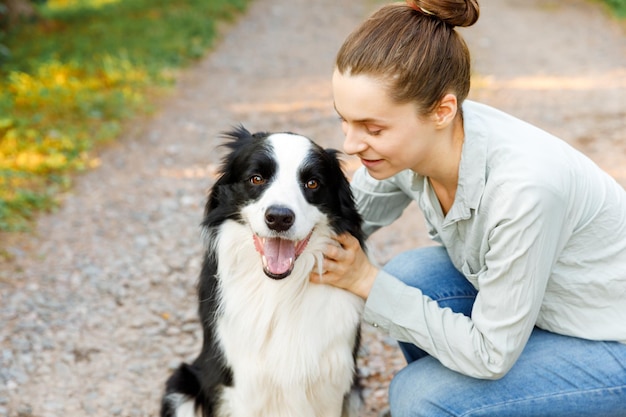 Lächelnde junge attraktive Frau, die mit niedlichem Hündchen-Border-Collie auf sommerlichem Hintergrund im Freien spielt