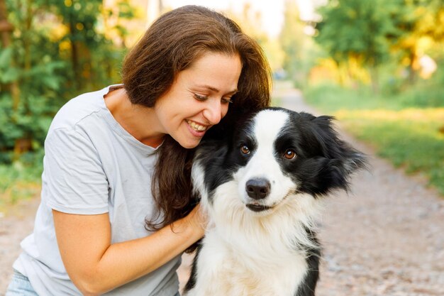 Lächelnde junge attraktive Frau, die mit niedlichem Hündchen-Border-Collie auf sommerlichem Hintergrund im Freien spielt