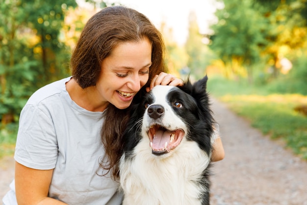 Lächelnde junge attraktive Frau spielt mit süßem Hündchen Border Collie im Sommer im Freien Backgroun...