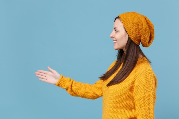 Lächelnde junge brünette Frau Mädchen in Pullover und Hut posiert isoliert auf blauem Hintergrund Studioportrait. People-Lifestyle-Konzept. Mock-up-Kopienbereich. Stehend mit ausgestreckter Hand zur Begrüßung.