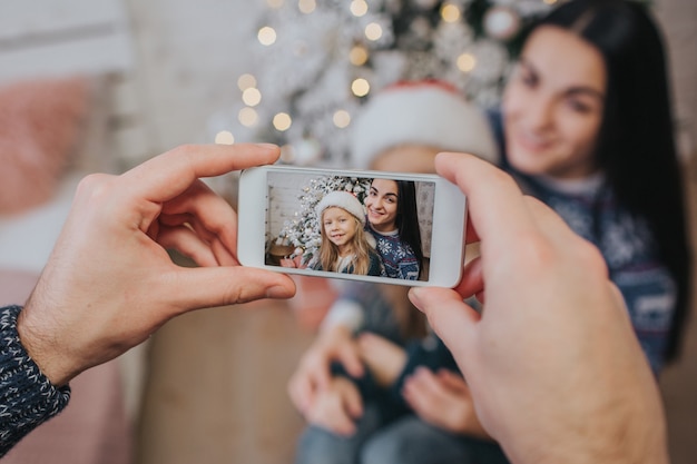 Lächelnde junge Familie in der Weihnachtsatmosphäre, die Foto mit Smartphone macht.