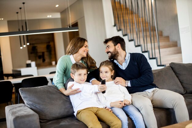 Lächelnde junge Familie vor dem Fernseher zusammen auf dem Sofa im Wohnzimmer