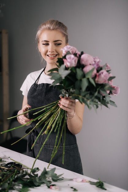 Lächelnde junge Floristin mit Schürze mit Blumenstrauß auf weißem Hintergrund