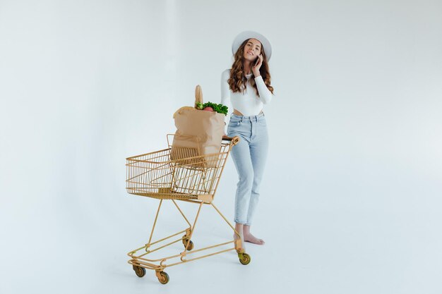 Lächelnde junge Frau, die Apfel hält und wegschaut, während sie mit Einkaufswagen steht