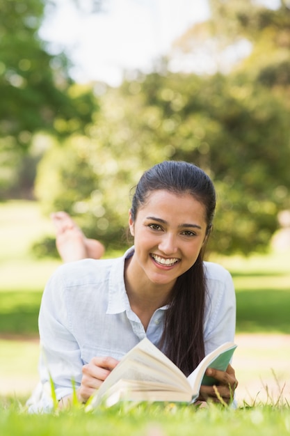 Lächelnde junge Frau, die ein Buch im Park liest