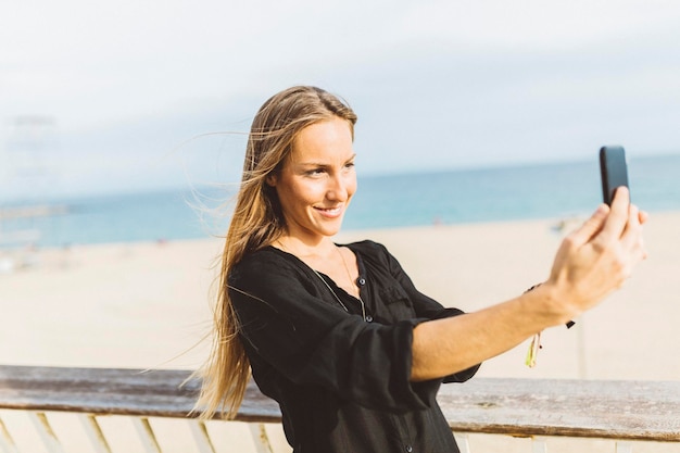 Lächelnde junge Frau, die ein Selfie am Strand macht