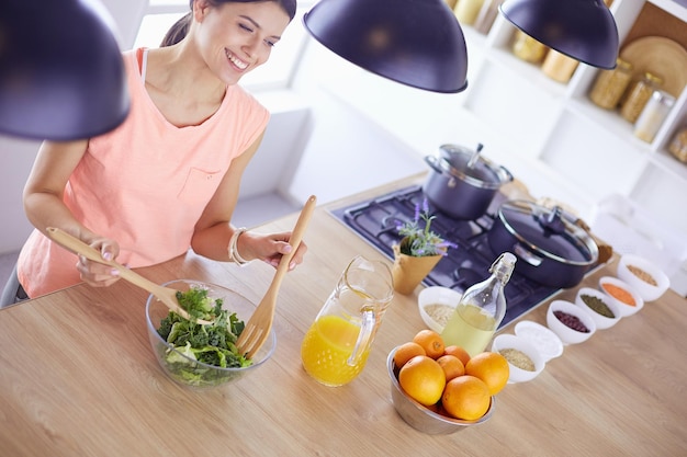 Foto lächelnde junge frau, die frischen salat in der küche mischt