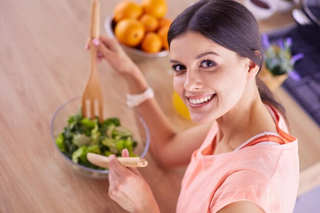 Lächelnde junge Frau, die frischen Salat in der Küche mischt