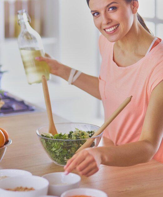 Lächelnde junge Frau, die frischen Salat in der Küche mischt