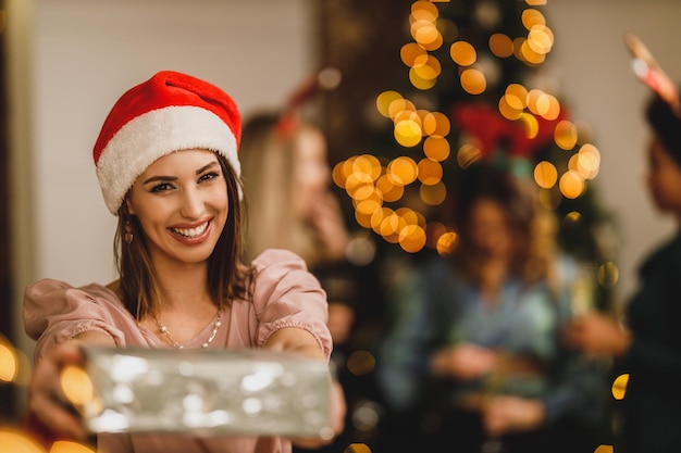 Lächelnde junge Frau, die Geschenke bringt, während sie Weihnachten mit ihren Freunden zu Hause feiert.