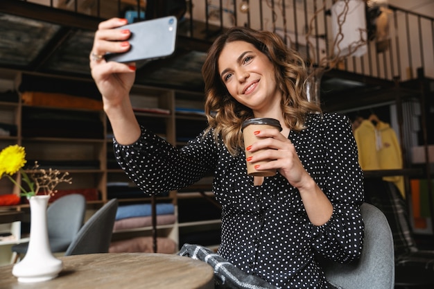 Lächelnde junge Frau, die im Café sitzt, Kaffee trinkt und ein Selfie macht