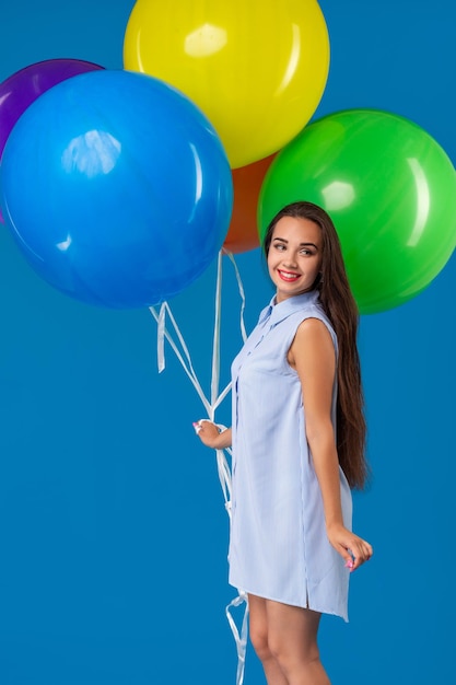 Lächelnde junge Frau, die Kamera schaut und bunte Luftballons über Blau isoliert hält
