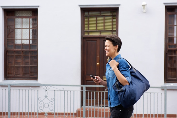 Foto lächelnde junge frau, die mit tasche und mobiltelefon geht