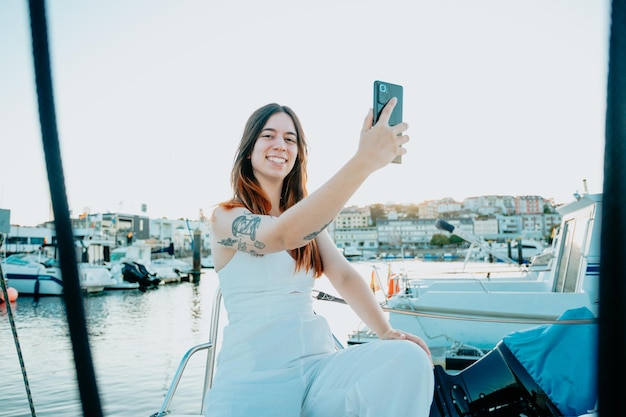 Lächelnde junge Frau, die Selfies auf einer Bootsyacht macht, die das Meer segelt Luxuslebensstil-KonzeptLächelndes Mädchen Verwenden Sie Social Media Streaming Service im Hintergrund Yachten und Schiffe