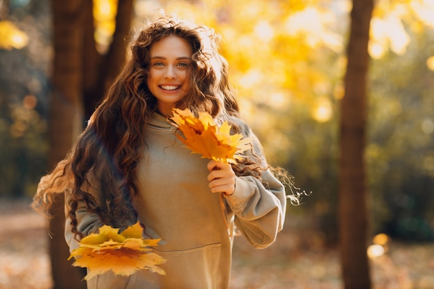 Lächelnde junge Frau genießt das Herbstwetter im Wald mit den gelben Blättern bei Sonnenuntergang