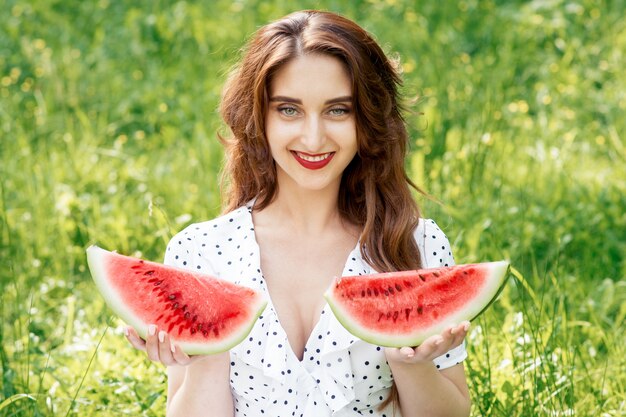 Lächelnde junge Frau hält zwei Scheiben Wassermelone.