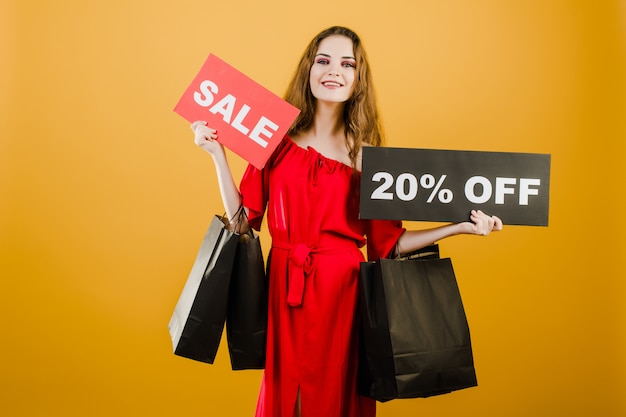 Lächelnde junge Frau hat Verkauf 20% weg vom Zeichen mit den bunten Einkaufstaschen, die über Gelb lokalisiert werden