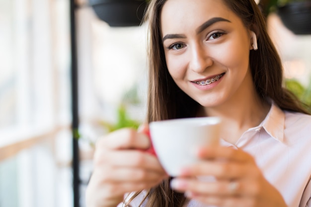 Lächelnde junge Frau im Café mit Kopfhörern, die Musik hören oder am Telefon sprechen