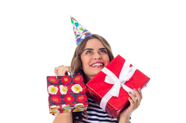 Lächelnde junge Frau in abgestreiftem T-Shirt und Festkappe, die Geschenke hält und im Studio auf weißen Hintergrund blickt