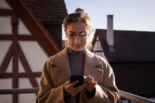 Lächelnde junge Frau in einem Mantel, der auf das Telefon schaut