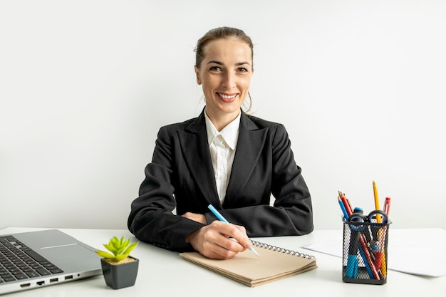Lächelnde junge Frau in einer Jacke, die in ein Notizbuch auf dem Desktop schreibt