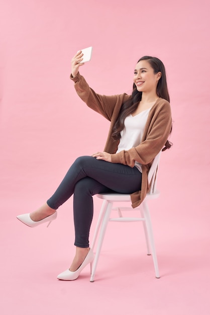 Lächelnde junge Frau macht Selfie-Foto auf dem Smartphone über rosa Hintergrund