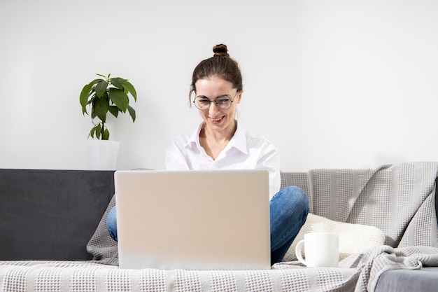 Lächelnde junge Frau mit Brille mit Laptop auf dem Sofa sitzend