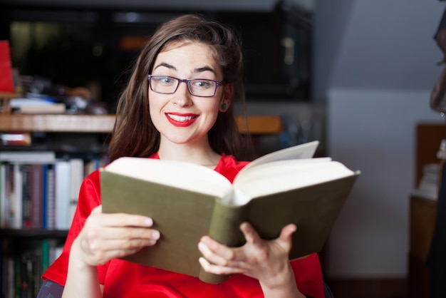 Lächelnde junge Frau mit Brille, während sie zu Hause ein Buch liest