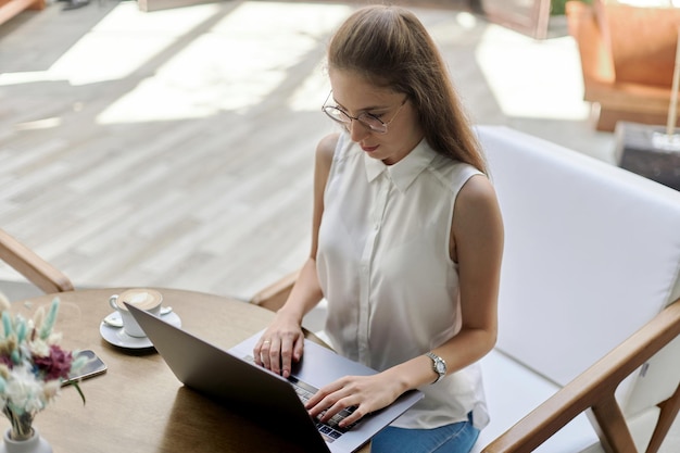 Lächelnde junge Frau mit einem Laptop an einem Tisch in einem Café