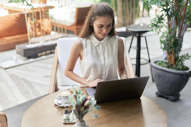 Lächelnde junge Frau mit einem Laptop an einem Tisch in einem Café