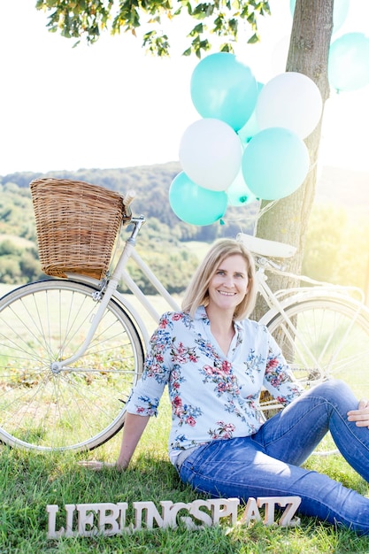 Foto lächelnde junge frau mit fahrrad sitzt auf dem gras