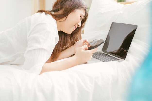 Foto lächelnde junge frau mit kreditkarte mit laptop und telefon im bett