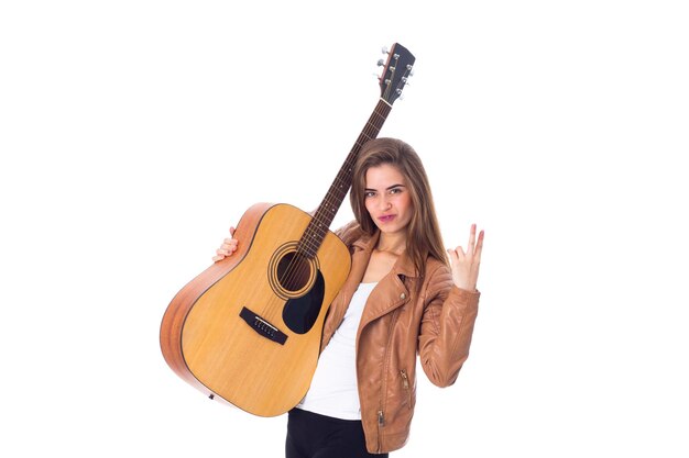 Lächelnde junge Frau mit langen Haaren in brauner Jacke und schwarzer Hose, die eine Gitarre hält und FRIEDEN auf weißem Hintergrund im Studio zeigt