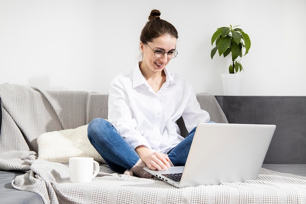 Lächelnde junge Frau mit Laptop mit Kaffee auf dem Sofa sitzend