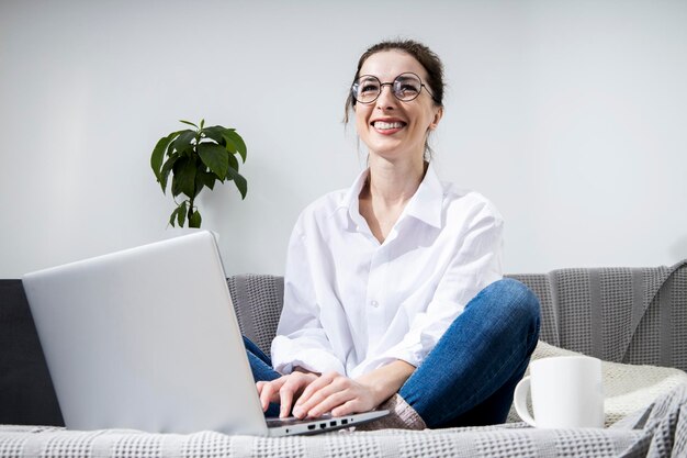 Lächelnde junge Frau mit Laptop mit Kaffee auf dem Sofa sitzend