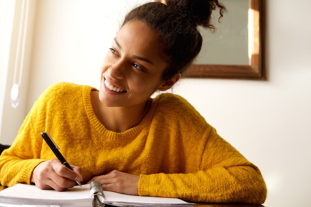 Lächelnde junge Frau mit Notizbuch und Stift am Schreibtisch