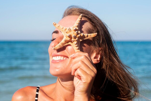 Lächelnde junge Frau schließt ihr Auge ein Seestern am Strand