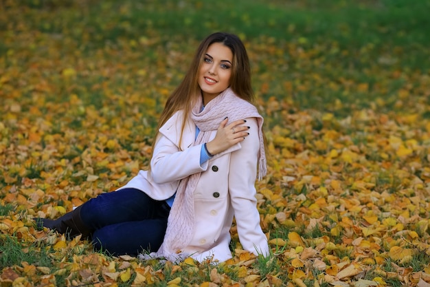 Lächelnde junge Frau sitzt auf dem Gras im Herbst. Herbst gelber Ahorngarten Hintergrund.