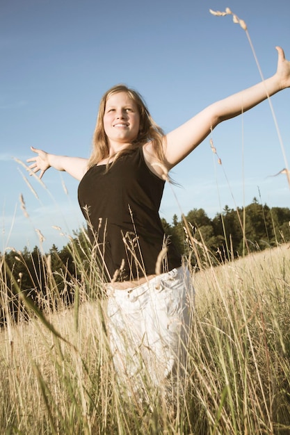 Foto lächelnde junge frau steht auf dem feld vor klarem himmel