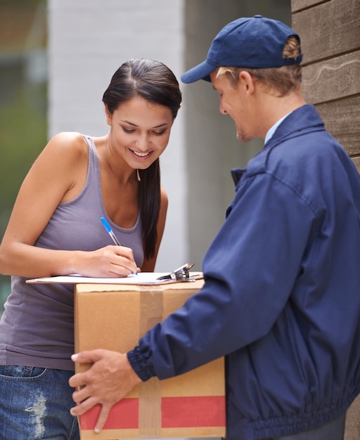 Lächelnde junge Frau und die Unterzeichnung der Lieferung vom Postboten oder des Austauschs für die Logistik oder die Zufriedenheit seines Kunden. Frachtbox und Dame an ihrer Haustür für ein Paket von einem Kurier oder einer Reederei