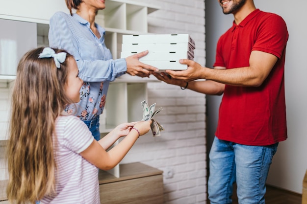 Lächelnde junge Frau und ihre Tochter erhalten zu Hause Pizza vom Lieferboten.