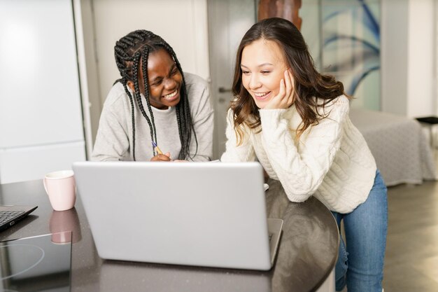 Lächelnde junge Frauen benutzen zu Hause einen Laptop auf dem Tisch