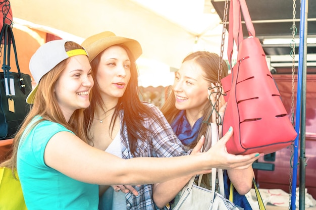 Foto lächelnde junge frauen, die ihre handtaschen auf dem flohmarkt überprüfen