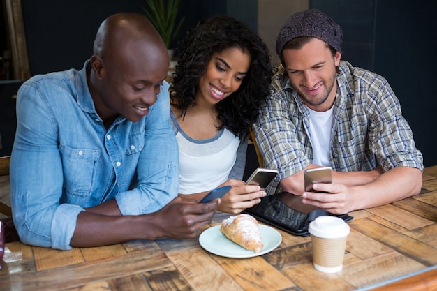 Lächelnde junge Freunde, die Smartphones am Tisch im Café verwenden