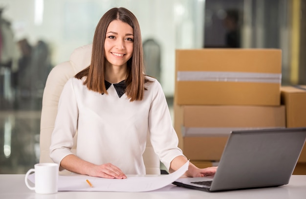 Lächelnde junge Geschäftsfrau, die im Büro nahe Kästen arbeitet.