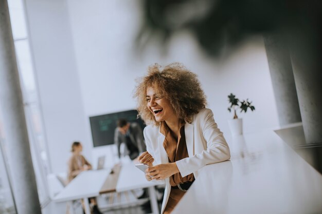 Lächelnde junge Geschäftsfrau mit Handy im modernen Büro