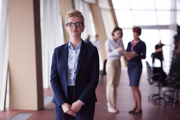 Foto lächelnde junge geschäftsfrau vor ihrem team, das im hintergrund verschwommen ist. gruppe junger geschäftsleute. modernes, helles startup-büro-interieur.