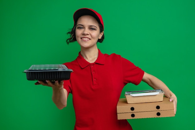 Lächelnde junge hübsche Lieferfrau mit Lebensmittelbehälter und Verpackung auf Pizzakartons
