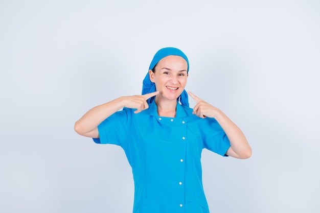 Lächelnde junge Krankenschwester zeigt ihr Lächeln mit Zeigefingern auf weißem Hintergrund